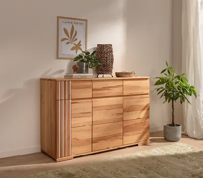 Stilvolle Kommode aus massiver Eiche mit dekorativen Lamellen, natürlich dekoriert mit Pflanzen und Korb-Lampe, platziert in hellem Raum mit grünem Teppich und Wandbild im skandinavischen Stil.